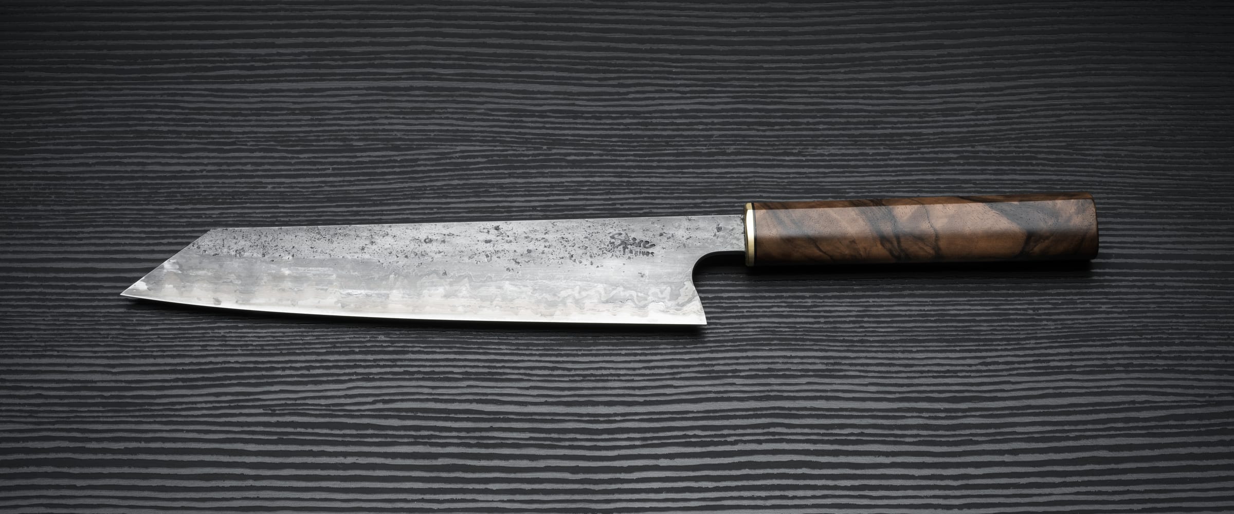 Handmade kitchen knives with hand-finished blades and wooden handles on a dark surface