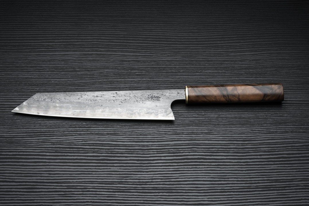 A handmade kitchen knife with a figured wooden handle on a dark surface