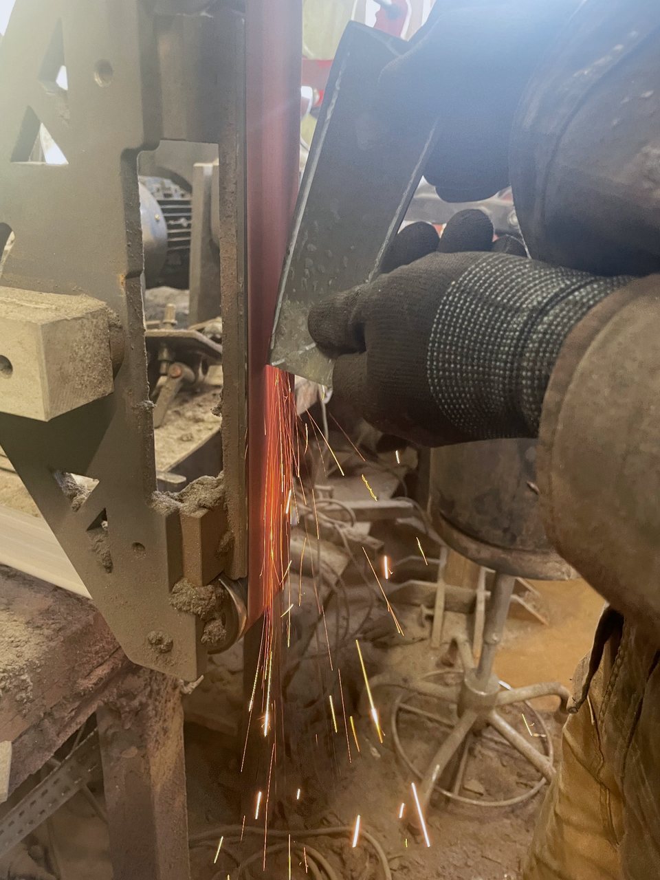 A gloved hand holds a knife blank against the grinding belt while sparks fly